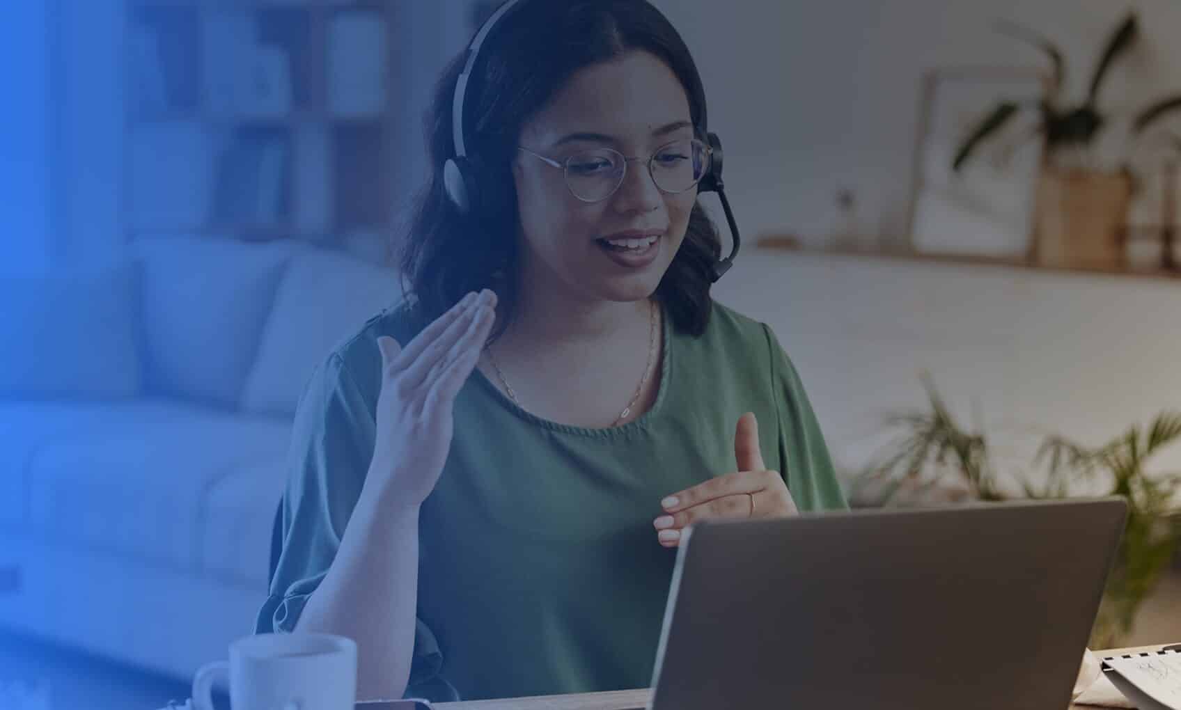 A woman with glasses and a headset sits at a desk, smiling and gesturing while discussing Azure Sentinel Implementation in a cozy, well-lit room.