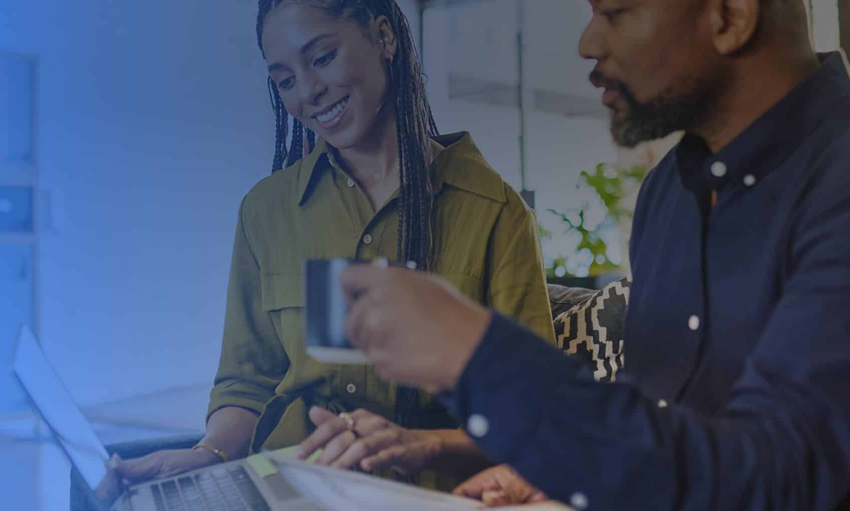 Two professionals, a woman and a man, sit at a table with a laptop, smiling and discussing Azure Migration in a bright, modern office setting.