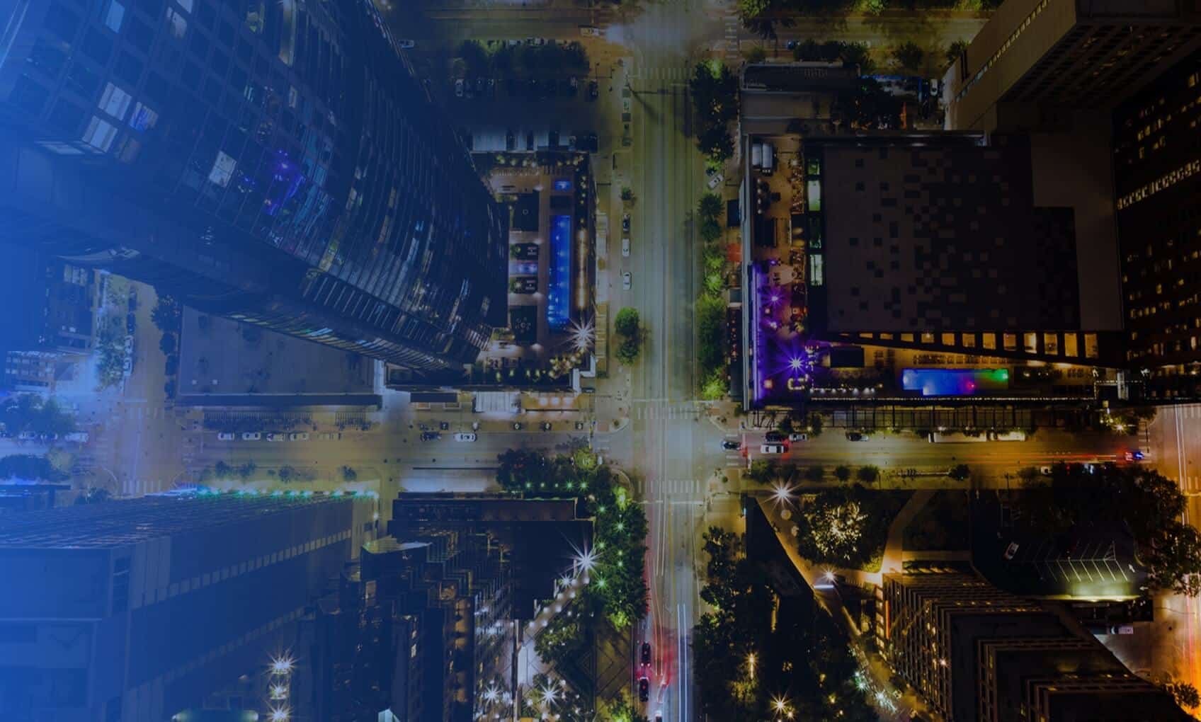 Aerial view of a city intersection at night, surrounded by tall buildings with illuminated windows and streets lit by streetlights—much like the seamless Azure Migration lighting up the digital landscape.