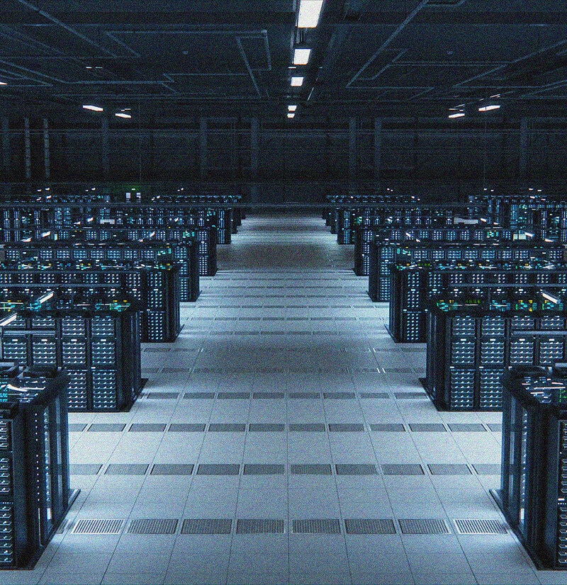 A large, brightly lit data center room filled with multiple rows of computer server racks, all illuminated by blue LED lights, showcasing advanced IT Asset Management along a wide central aisle beneath a high ceiling.