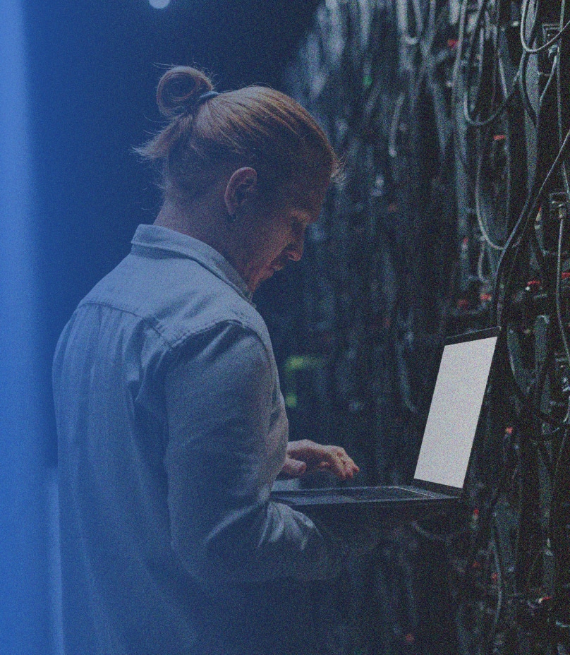 man working on a laptop with a wall full of cords