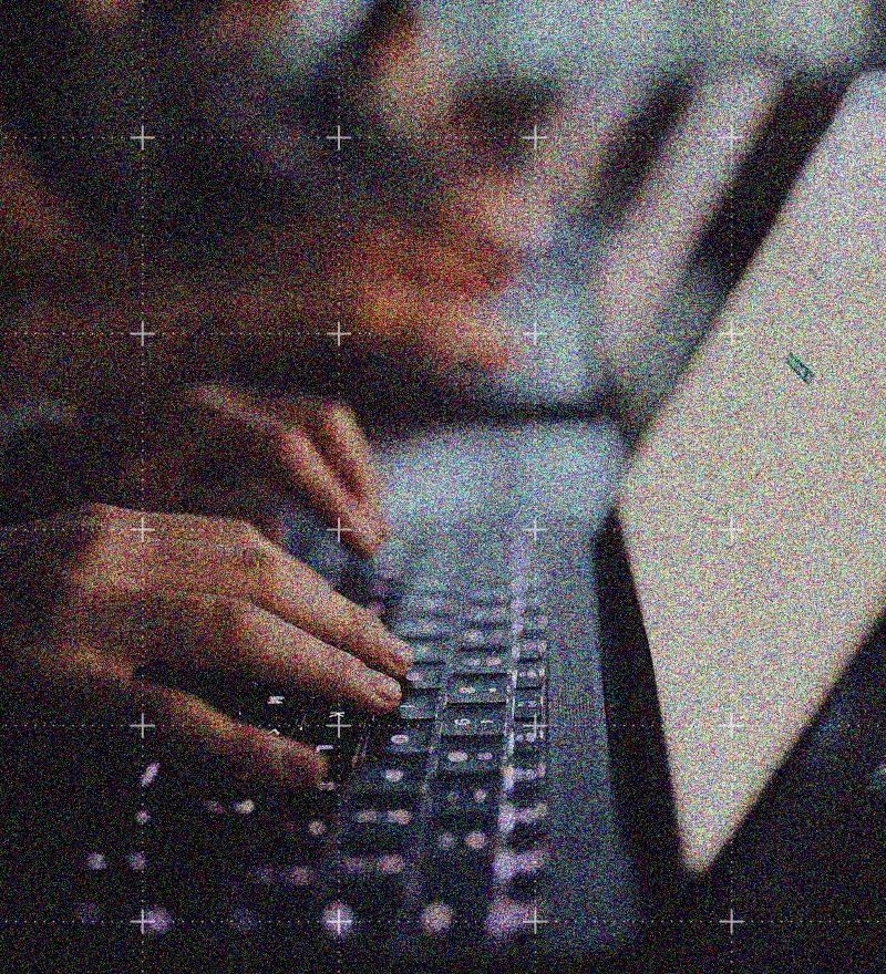 Close-up of hands typing on a laptop keyboard, with the screen slightly visible and blurred in the background. The image has a grainy, noisy texture, evoking the fast-paced environment of IT Solutions professionals at work.