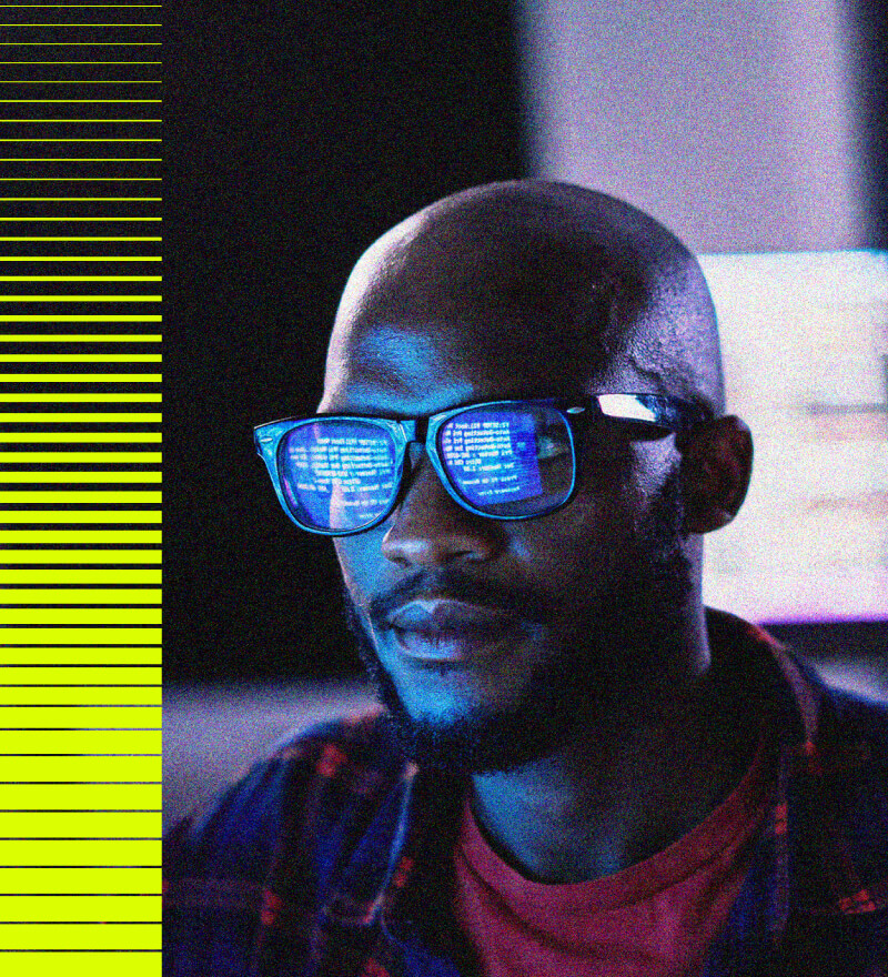 A person wearing glasses reflects computer code on the lenses, with blue light from a monitor illuminating their face. On the left side, there are horizontal yellow and black lines in a digital style pattern.