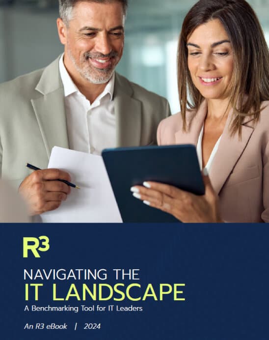 A man and a woman in business attire smile while looking at a tablet. Below them is a blue banner with the text “Navigating the IT Landscape – A Benchmarking Tool for IT Leaders. An R3 eBook | 2024.”.