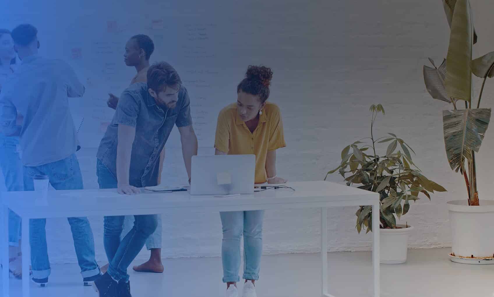 A group of people work together in a bright office. Two people stand at a white desk focused on Azure Sentinel Implementation, while four others talk near a whiteboard. Green potted plants decorate the space.